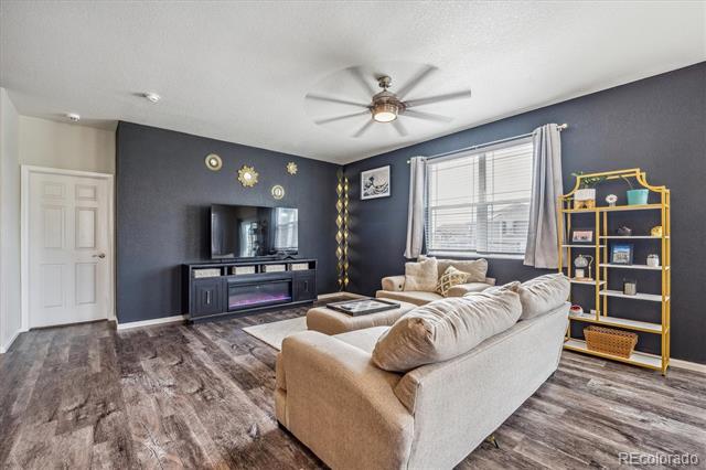 Living room with a beige sectional, electric fireplace, and gold shelving against dark blue walls.
