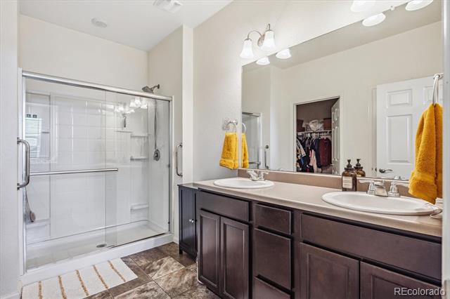 Bathroom with a dark double-sink vanity and large glass-enclosed tiled shower.
