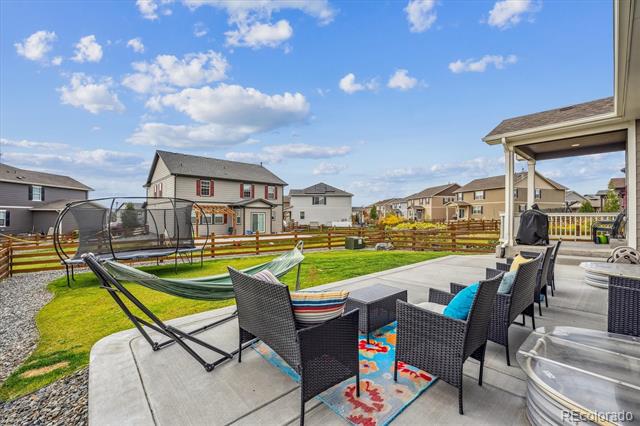 Backyard patio with black wicker seating and a hammock overlooking a fenced lawn and neighboring homes.