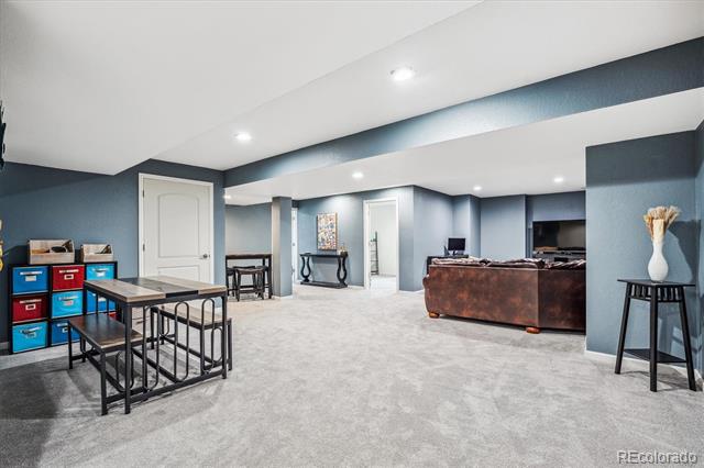 Finished basement family room with a brown sectional, game table, and colorful storage bins.