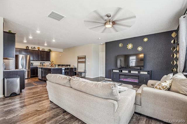 Open-plan living room with a light sectional, dark television wall, fireplace, and kitchen beyond.