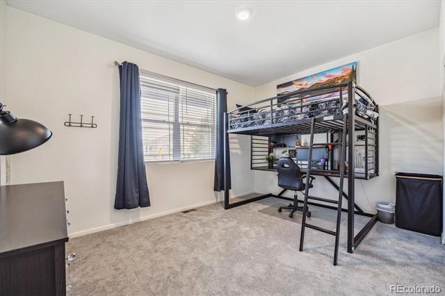 Bedroom with a metal loft bed, desk, and blue curtains beside a large window.