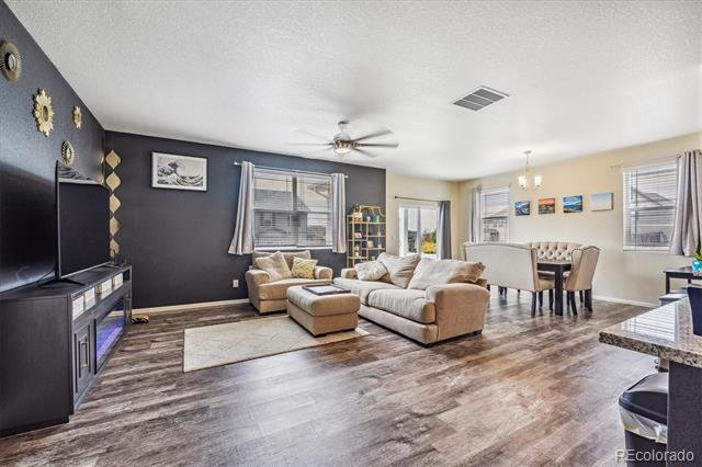 Living room with beige sectional and dark television wall, opening to a dining area by the windows.