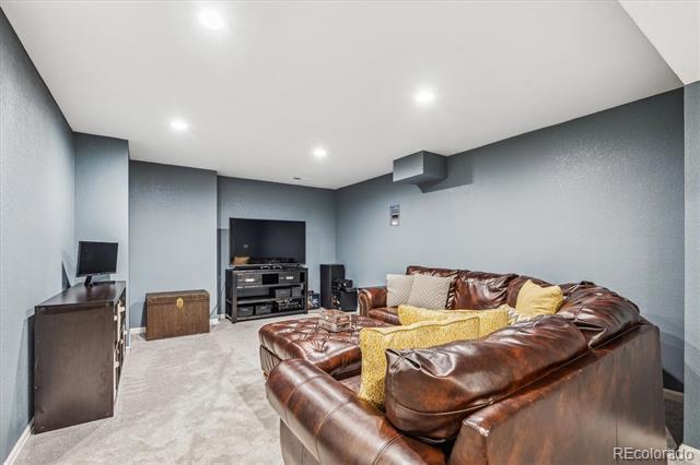 Furnished media room with a brown leather sectional, yellow cushions, and television.