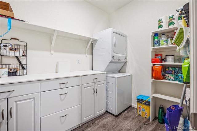 Laundry room with white cabinets, stacked washer and dryer, and open storage shelving.