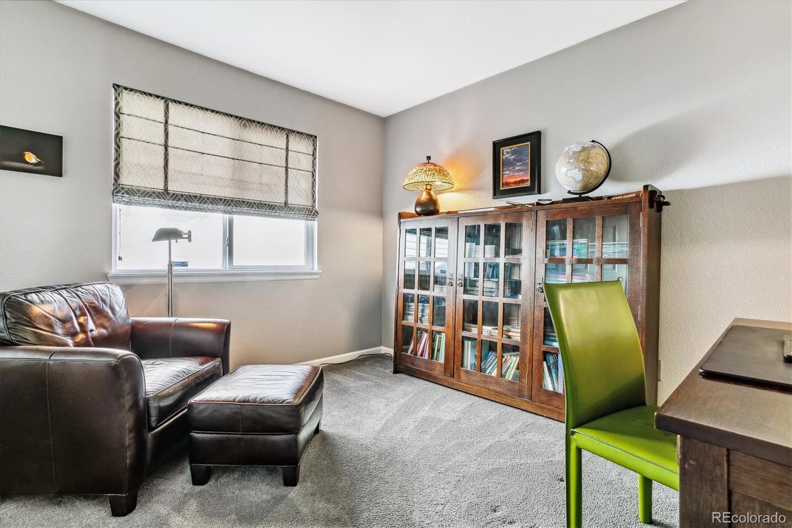 Furnished home office with leather seating, a glass-front bookcase, and a bright green chair.