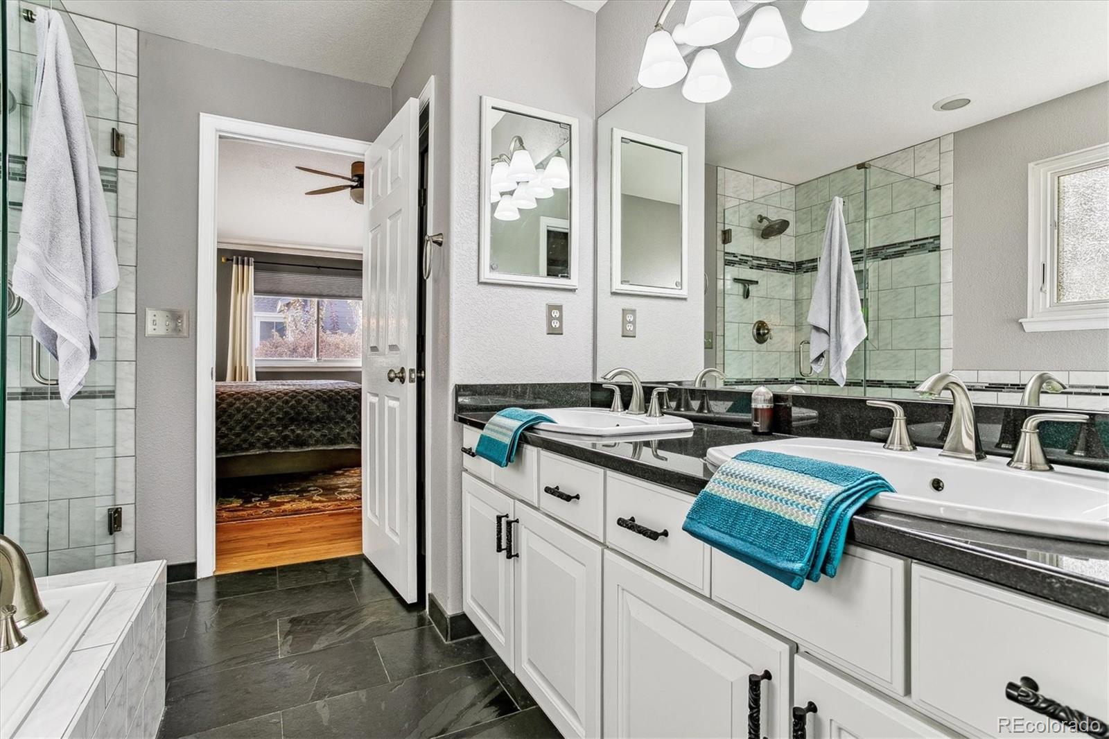 Bathroom with a double vanity, glass shower, dark tile floor, and turquoise towels.