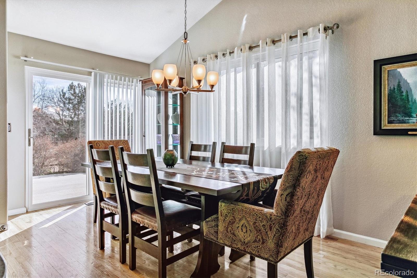 Dining room with a dark wood table, chandelier, sheer curtains, and sliding glass door.