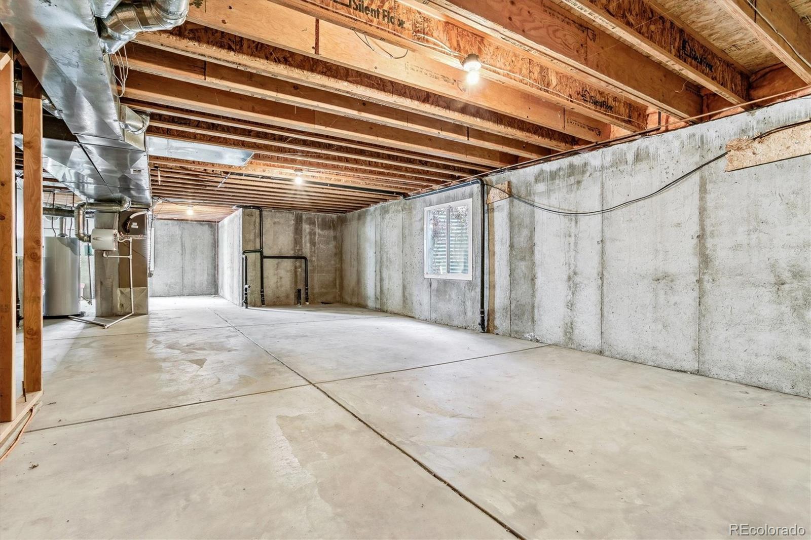 Unfinished basement with exposed ceiling joists, concrete walls, and visible HVAC equipment.