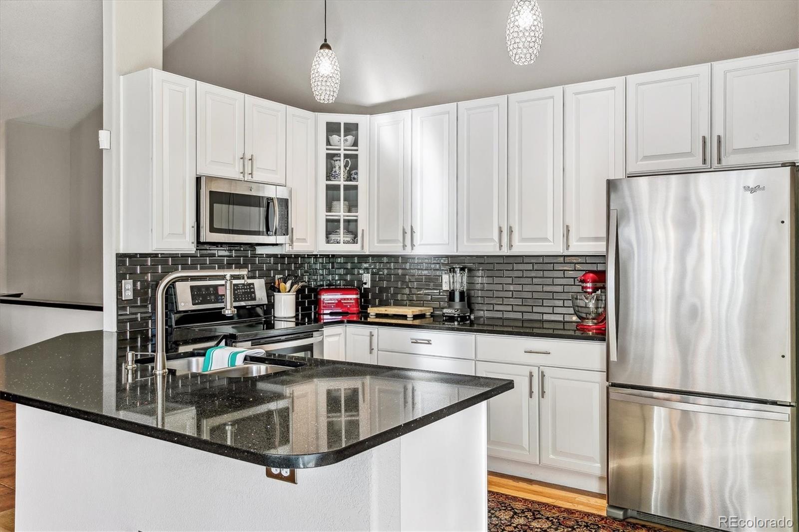 Kitchen with white cabinets, black tile backsplash, granite island, and stainless steel appliances.