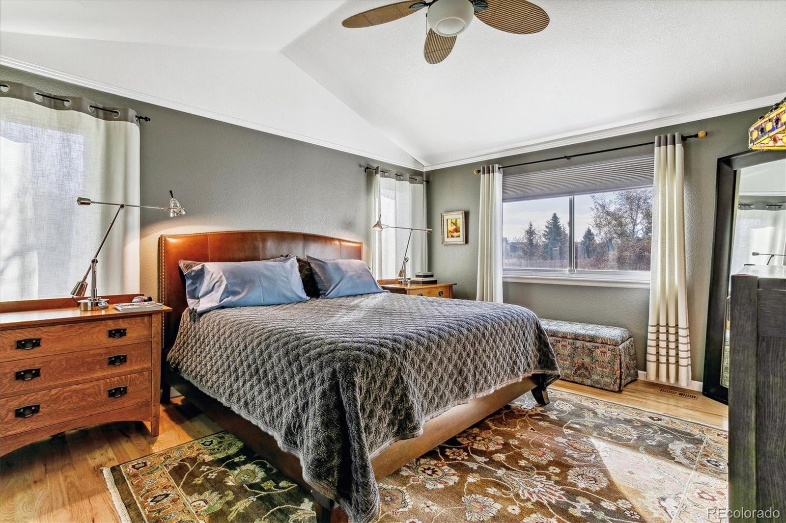 Furnished bedroom with a large bed, curved leather headboard, patterned rugs, and a window overlooking trees.