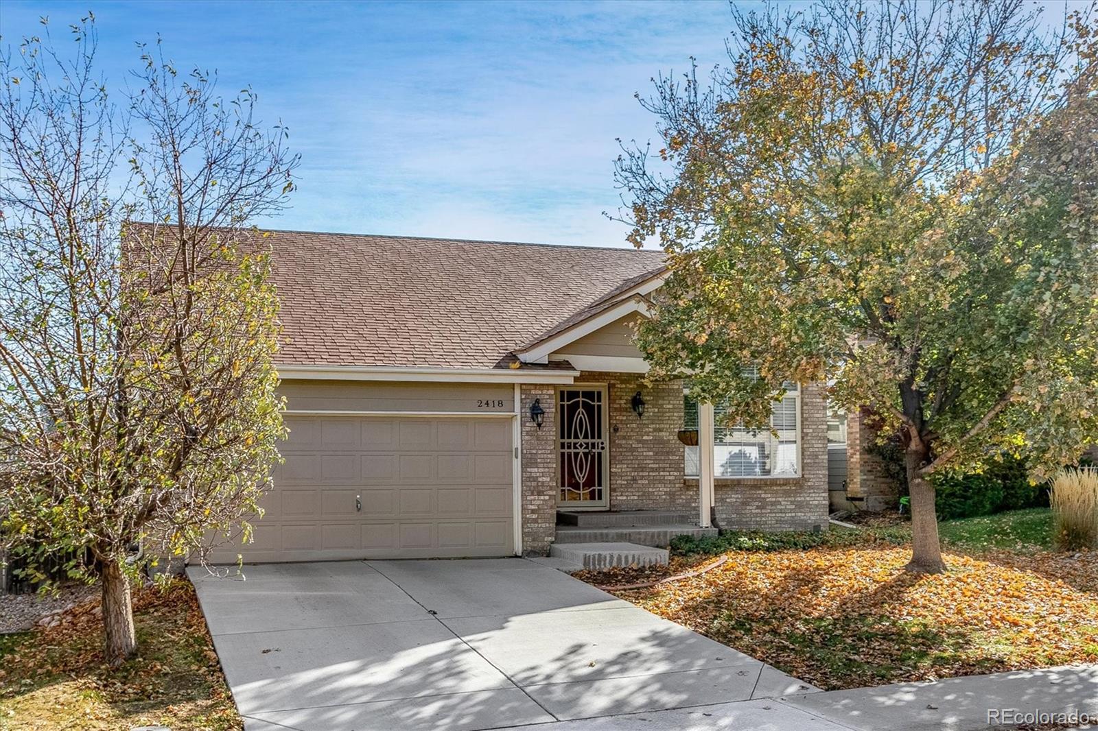 Brick home with a two-car garage and autumn trees along the driveway.