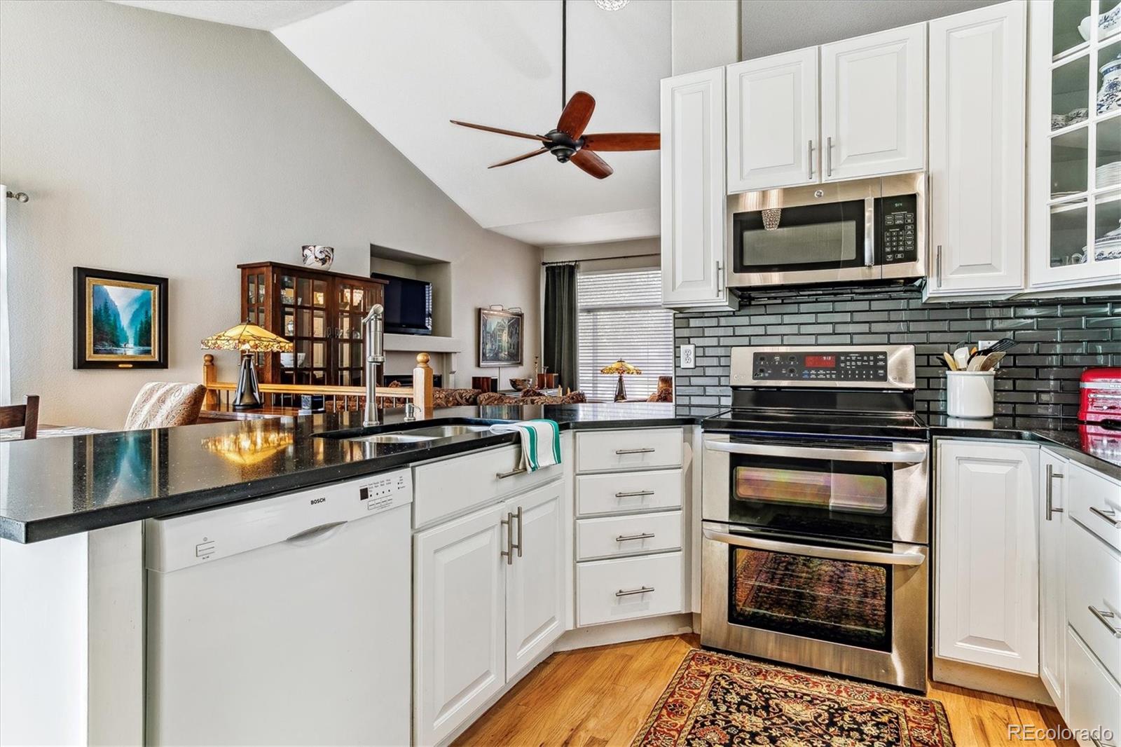 Kitchen with white cabinets, black counters, dark green tile backsplash, and stainless steel appliances.