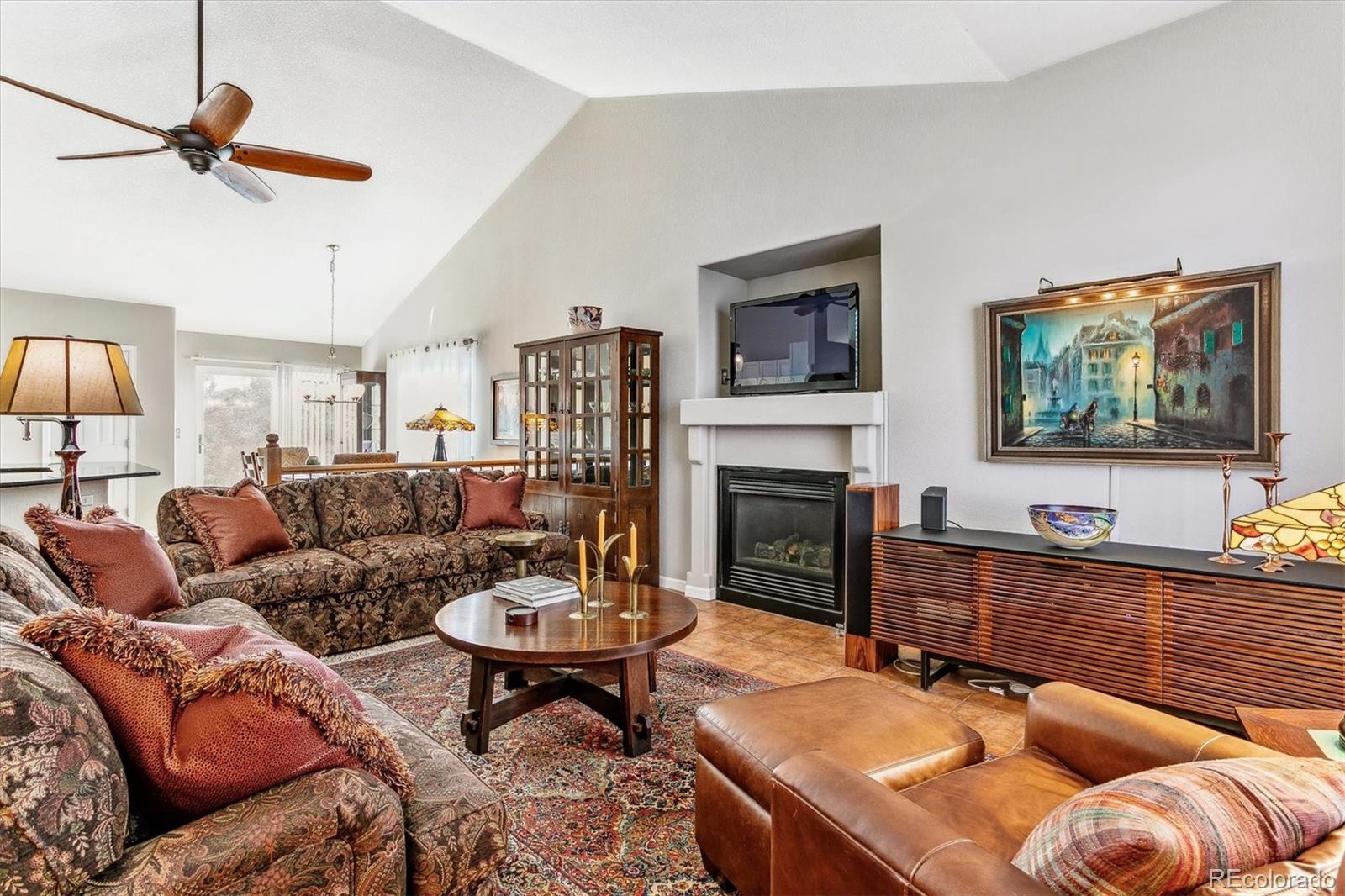 Living room with a vaulted ceiling, gas fireplace, patterned sofas, and dining area beyond.