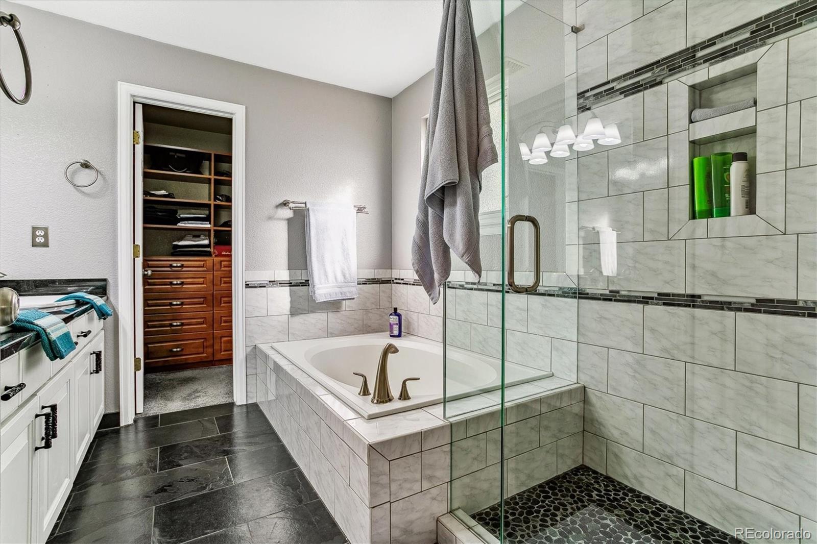 Bathroom with a glass walk-in shower and tiled soaking tub beside an open walk-in closet.