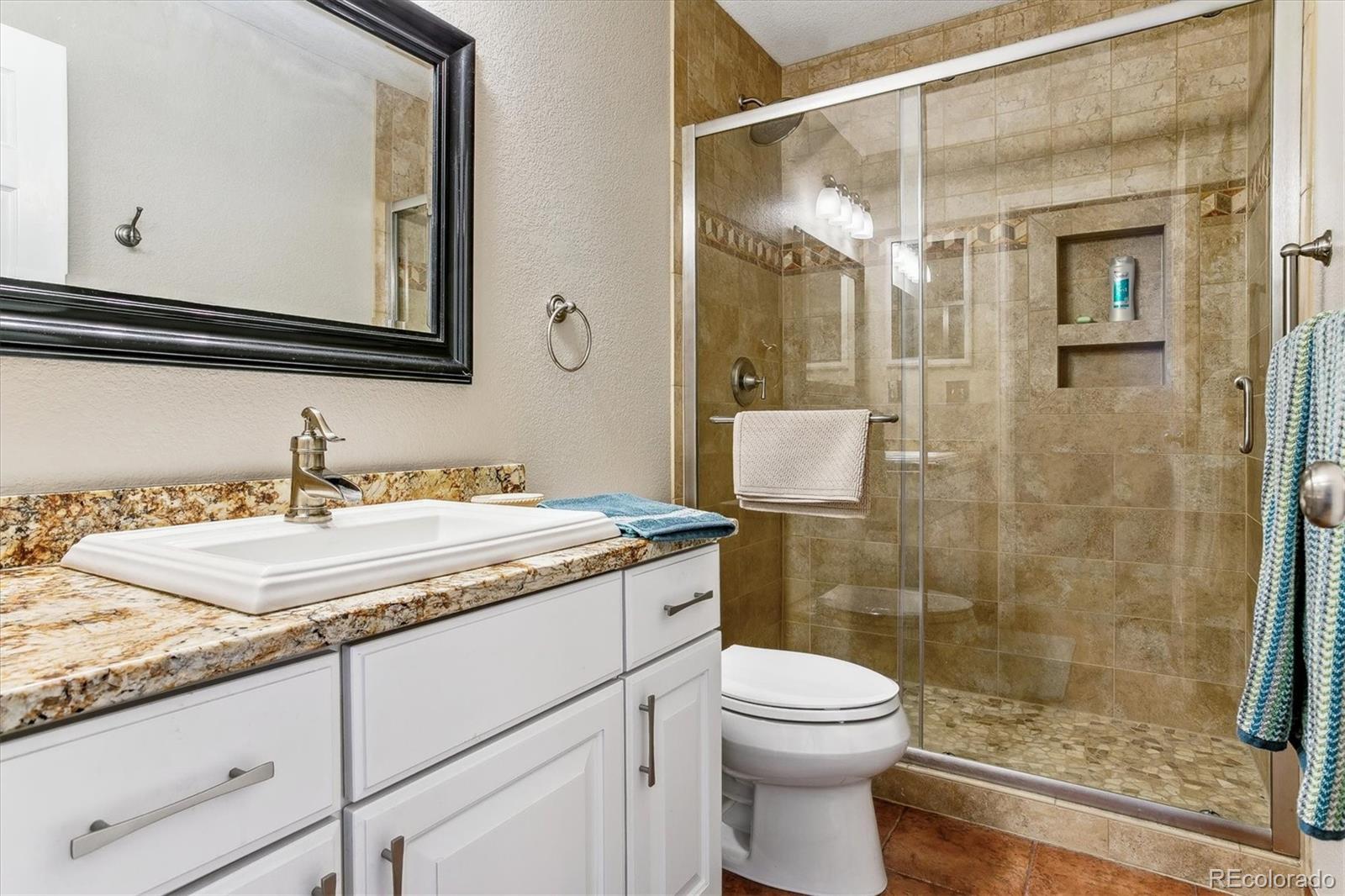 Bathroom with a granite-topped white vanity and glass-enclosed tan tile shower.