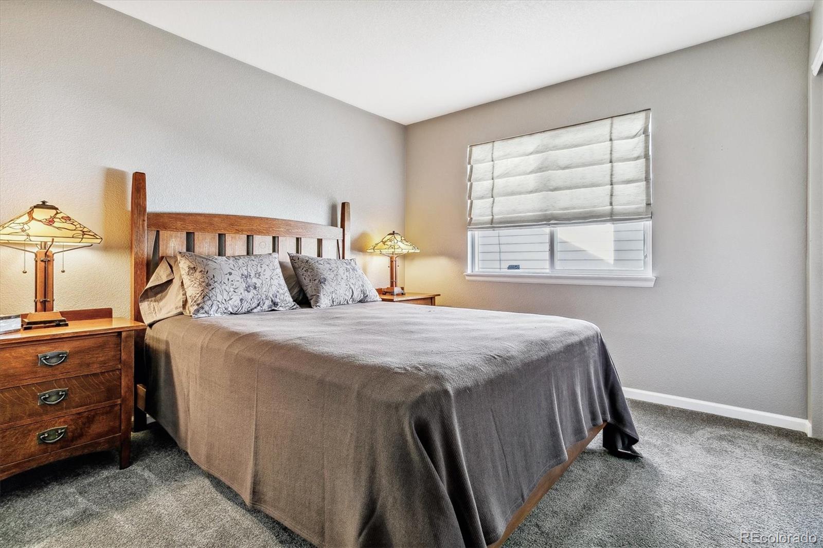 Bedroom with a wooden bed, gray bedding, matching nightstands, and a window with a Roman shade.