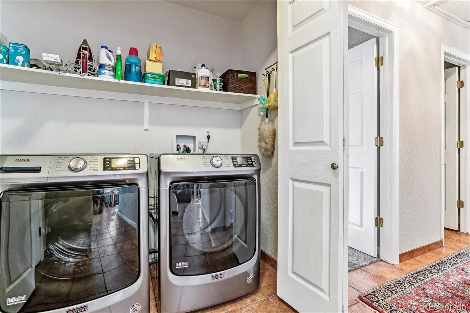 Laundry room with two front-loading Maytag appliances and a shelf of cleaning supplies.