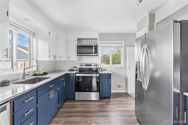 Bright kitchen with navy cabinets, stone countertops, stainless-steel appliances, and windows.