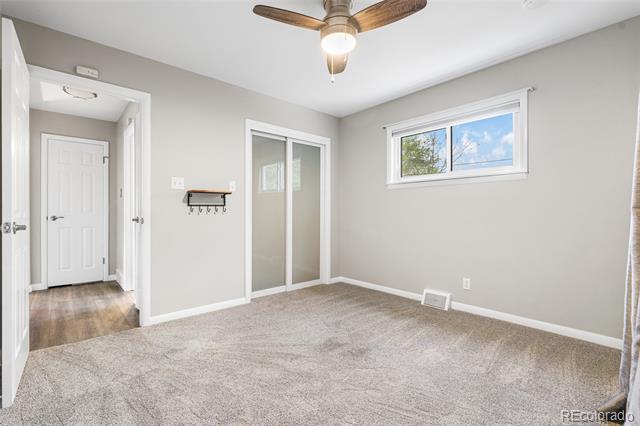 Empty bedroom with beige carpet, a ceiling fan, and a sliding closet door.