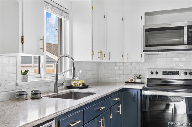 Kitchen with navy lower cabinets, white upper cabinets, stone counters, and stainless steel appliances.