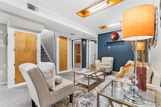 Staged basement living room with white seating, glass coffee tables, and a dark teal accent wall.