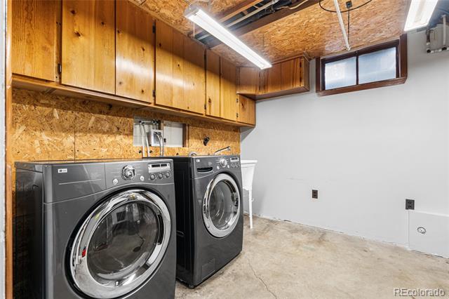 Laundry room with a front-loading washer and dryer beneath wood cabinets and an unfinished ceiling.