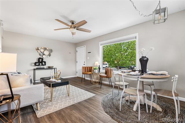 Staged living and dining area with a round set table beside a large window overlooking green foliage.