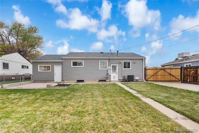 Rear of a gray-sided single-story house beyond a grassy yard and concrete walkway.