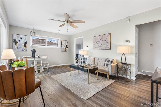 Staged living room with a ceiling fan, patterned rug, sofa, and adjoining dining area.