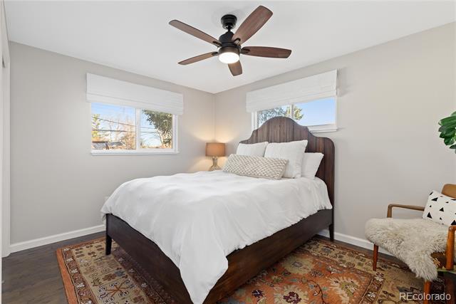 Bedroom with white bedding, a dark wood bed, two windows, and a patterned rug.