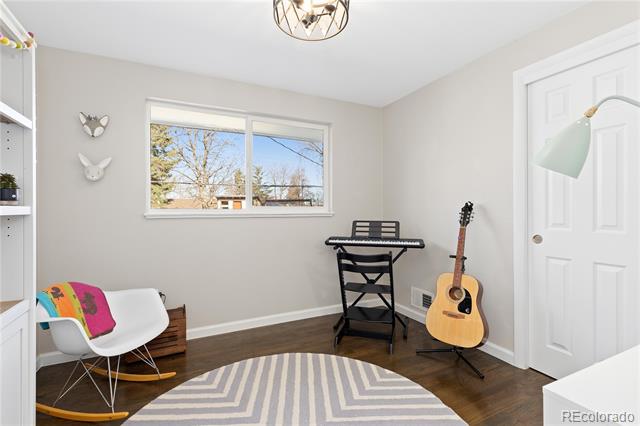 Music room with a keyboard, acoustic guitar, colorful chair cushion, and wide window overlooking trees.