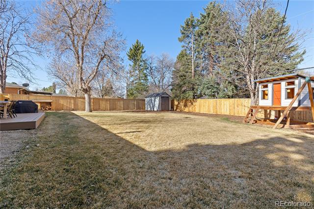 Backyard with a wooden privacy fence, small shed, raised deck, and children's play structure.