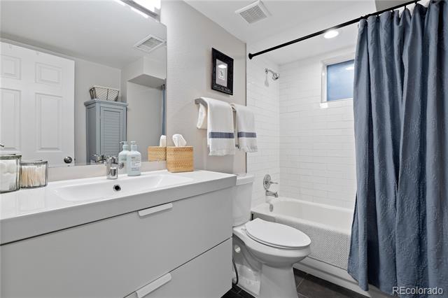Bathroom with white vanity and tiled tub, partly covered by a navy blue shower curtain.