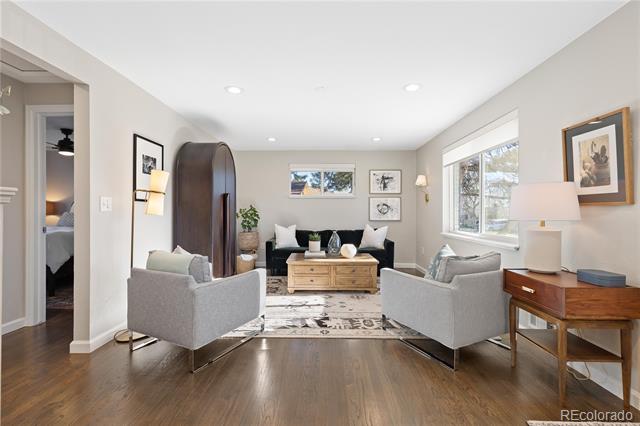 Staged living room with gray armchairs, a dark sofa, hardwood floors, and large windows.