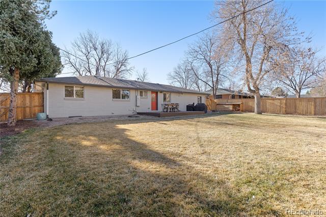 Single-story home with a red rear door and patio, viewed across a broad fenced backyard.
