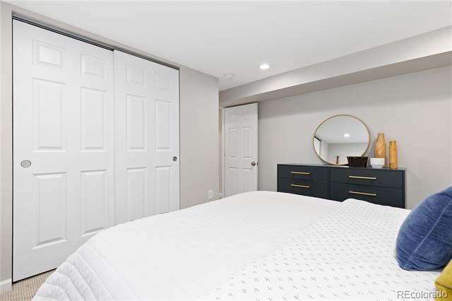 Bedroom with a white bed, paneled closet doors, and a dark dresser beneath a round mirror.