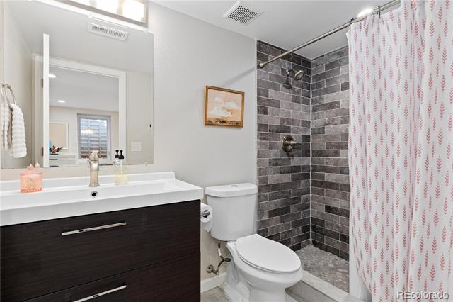 Bathroom with a dark wood vanity and gray tiled shower behind a patterned curtain.