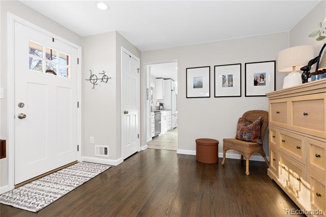 Home entryway with a white front door, dark wood floors, and a wicker chair beside a dresser.