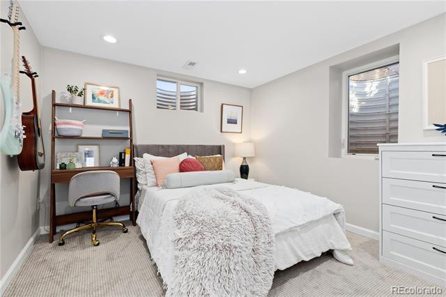 Bedroom with a white bed, fluffy throw, desk, open shelving, and guitars on the wall.