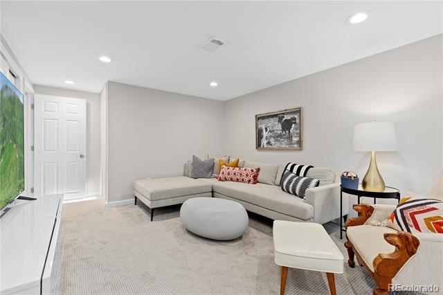 Staged living room with a gray sectional, patterned pillows, round ottoman, and wall-mounted television.