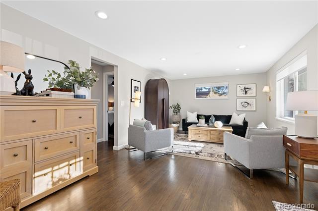 Staged living room with dark hardwood floors, a black sofa, gray armchairs, and large windows.