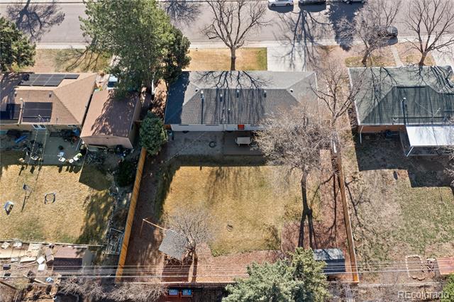 Aerial view of a fenced backyard behind a single-story home, with a patio and mature trees.