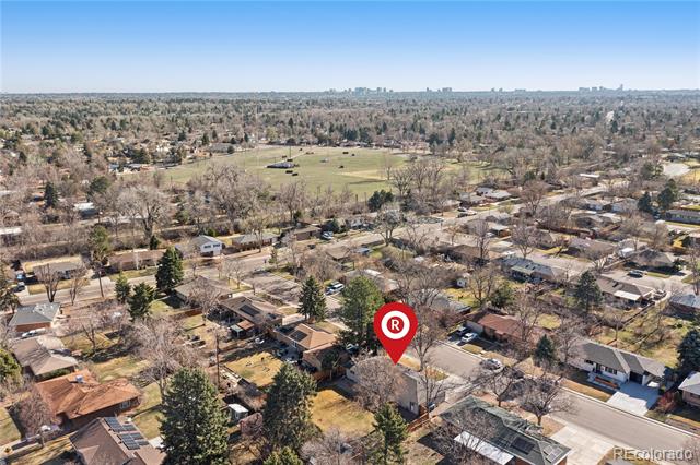 Aerial view of a residential neighborhood, with a large open field and distant city skyline.