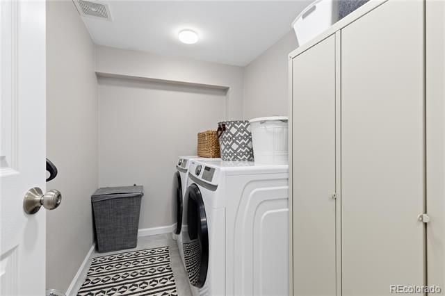 Laundry room with a white front-loading washer and dryer beside tall storage cabinets and a patterned runner.