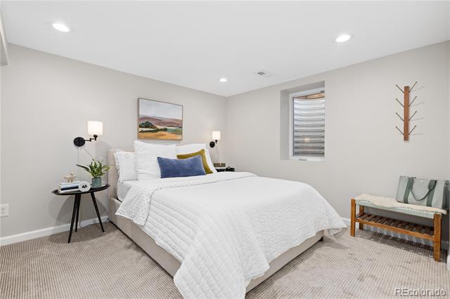 Staged bedroom with a white quilted bed and cushioned bench beside a small window.