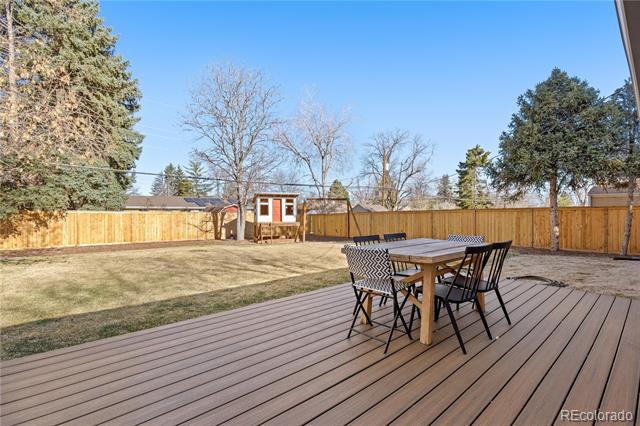 Backyard deck with outdoor dining set overlooking a fenced lawn and mature trees.