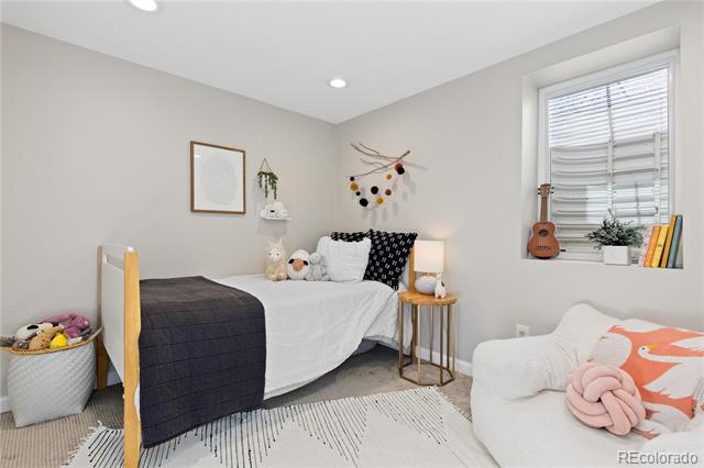 Bedroom with a white bed, charcoal blanket, window seat, and white lounge chair with a coral pillow.