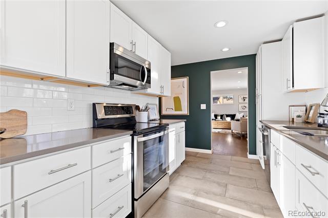 Kitchen with white cabinets, stainless steel appliances, dark countertops, and a teal accent wall.