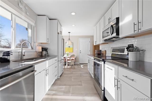 Bright white galley kitchen with stainless steel appliances, large windows, and a dining nook at the far end.